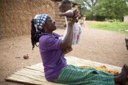 African mother sitting on a mat holding up her baby.