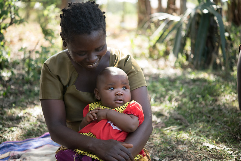 African mother smiles and looks down at her baby dressed in a red dress in her arms.